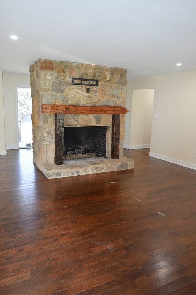 unfurnished living room featuring a stone fireplace and dark hardwood / wood-style floors