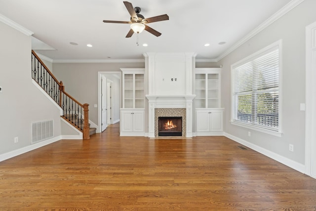 unfurnished living room with built in shelves, ornamental molding, a tile fireplace, hardwood / wood-style flooring, and ceiling fan