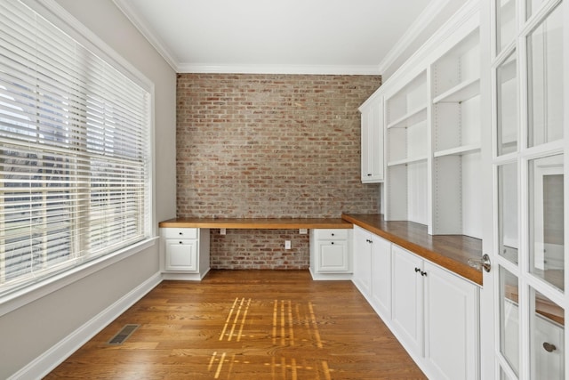 kitchen featuring white cabinetry, built in desk, wooden counters, and brick wall