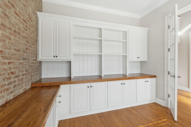 kitchen with white cabinetry, brick wall, butcher block counters, and light hardwood / wood-style floors