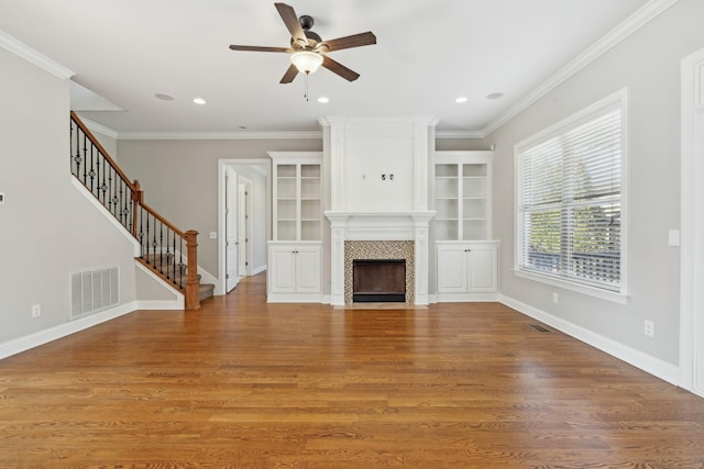 unfurnished living room with ornamental molding, built in features, ceiling fan, a fireplace, and hardwood / wood-style floors