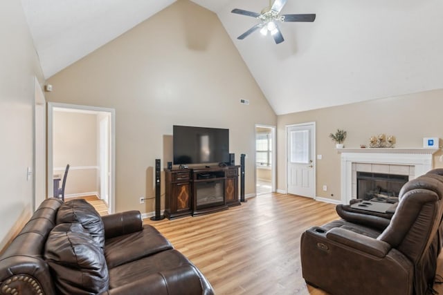 living room featuring ceiling fan, high vaulted ceiling, a fireplace, and light hardwood / wood-style floors