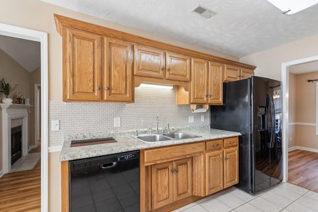 kitchen with sink, black appliances, light tile patterned floors, a tiled fireplace, and backsplash