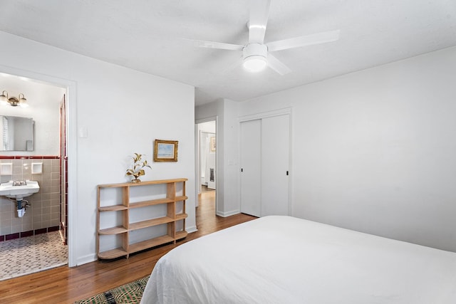 bedroom with connected bathroom, sink, wood-type flooring, a closet, and ceiling fan