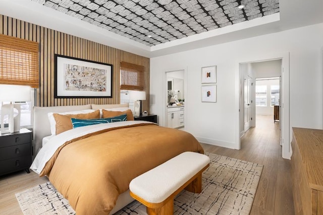 bedroom featuring brick ceiling, ensuite bath, and light hardwood / wood-style flooring