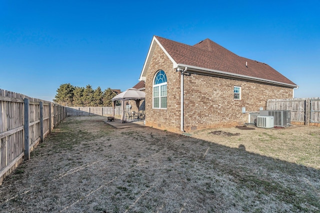 view of property exterior with a fenced backyard, central air condition unit, brick siding, a gazebo, and crawl space