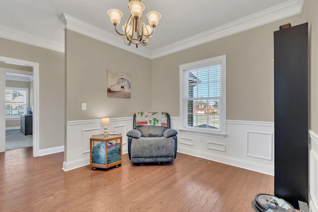 sitting room with a notable chandelier, visible vents, ornamental molding, wainscoting, and wood finished floors