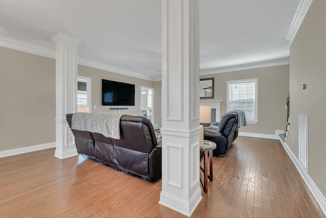 living area with crown molding, a fireplace, decorative columns, and wood finished floors