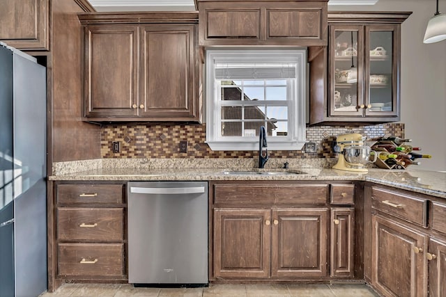 kitchen with decorative backsplash, glass insert cabinets, light stone countertops, stainless steel appliances, and a sink