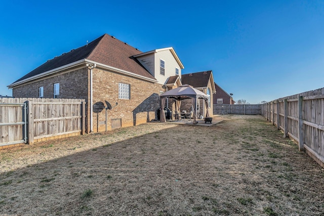 rear view of property featuring brick siding, a patio, a fenced backyard, and a gazebo