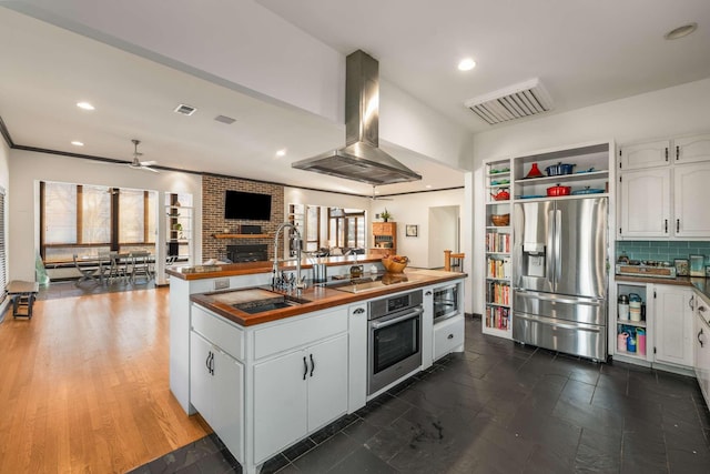 kitchen with a fireplace, sink, white cabinets, island exhaust hood, and stainless steel appliances