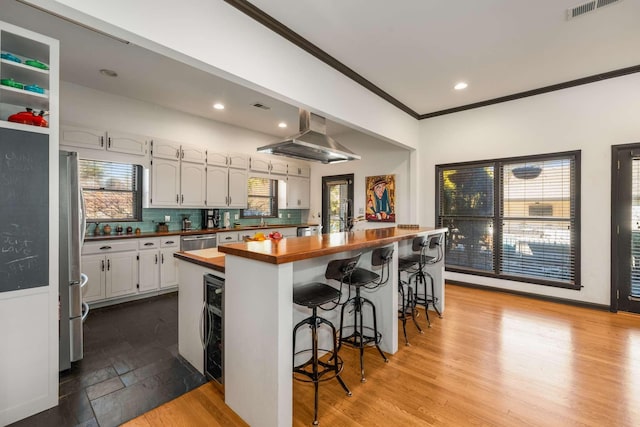 kitchen with butcher block countertops, tasteful backsplash, white cabinetry, exhaust hood, and stainless steel appliances