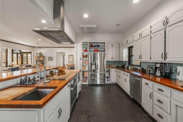 kitchen with butcher block counters, sink, white cabinetry, island range hood, and appliances with stainless steel finishes