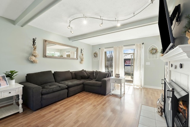 living room featuring a tiled fireplace, beam ceiling, and light hardwood / wood-style flooring