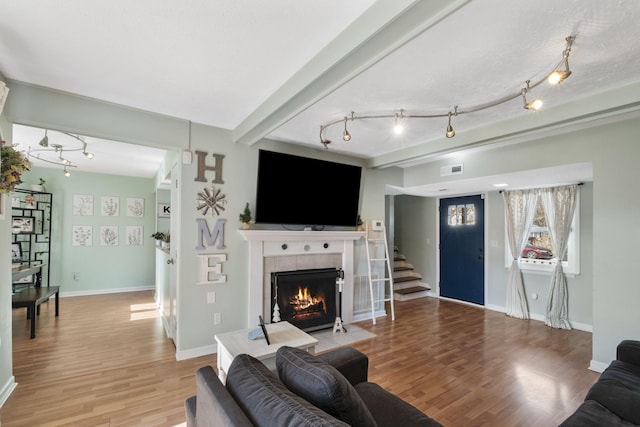 living room featuring beamed ceiling, a tiled fireplace, light hardwood / wood-style floors, and a textured ceiling