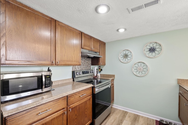 kitchen with stainless steel appliances, a textured ceiling, light hardwood / wood-style flooring, and backsplash