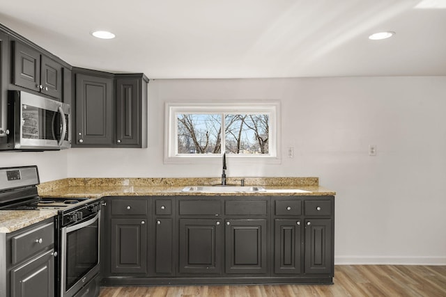 kitchen with sink, light hardwood / wood-style flooring, light stone countertops, and appliances with stainless steel finishes