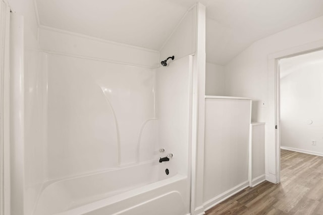 bathroom with hardwood / wood-style floors, vaulted ceiling, and tub / shower combination