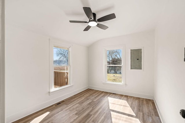 empty room featuring vaulted ceiling, electric panel, ceiling fan, and light hardwood / wood-style flooring