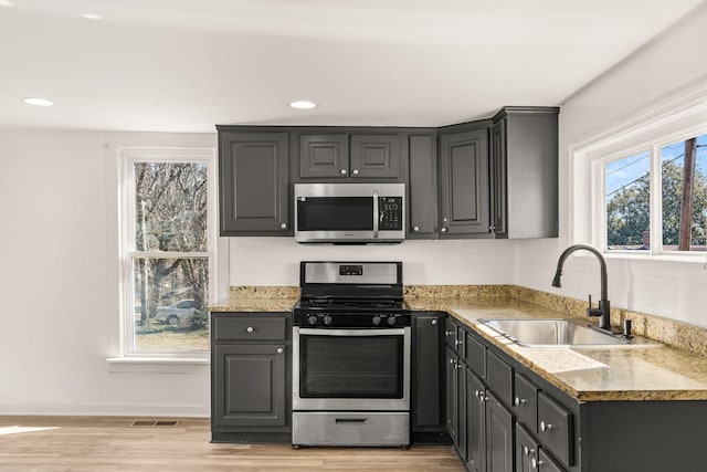 kitchen with appliances with stainless steel finishes, light stone countertops, sink, and light hardwood / wood-style flooring