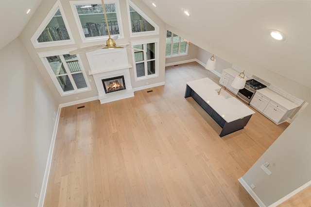 unfurnished living room featuring high vaulted ceiling and light wood-type flooring