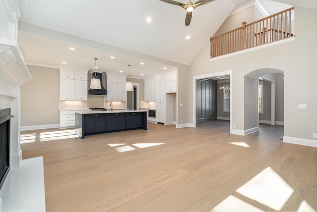 unfurnished living room featuring sink, ceiling fan with notable chandelier, high vaulted ceiling, and light hardwood / wood-style floors