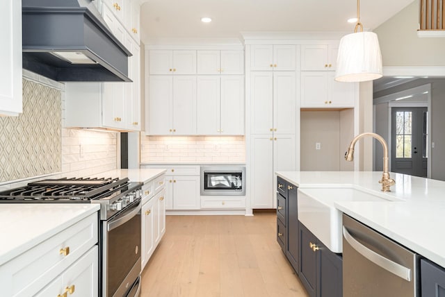 kitchen with decorative light fixtures, white cabinetry, sink, custom exhaust hood, and stainless steel appliances