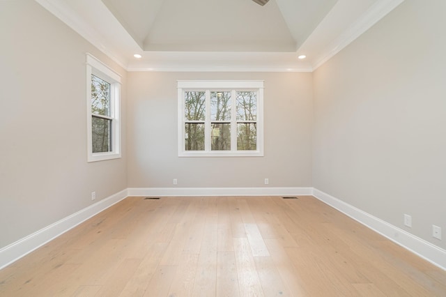 empty room featuring vaulted ceiling, ornamental molding, light hardwood / wood-style floors, and a tray ceiling