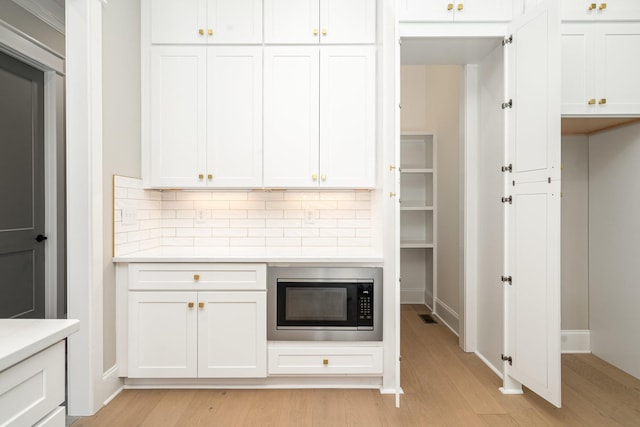 kitchen featuring white cabinetry, stainless steel microwave, tasteful backsplash, and light wood-type flooring