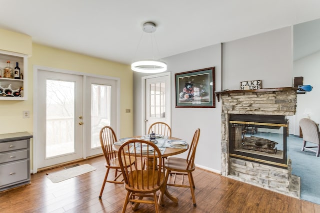 dining space featuring wood finished floors, visible vents, baseboards, a fireplace, and french doors