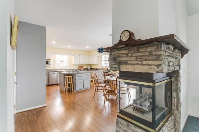 interior space with baseboards, white cabinetry, a stone fireplace, hardwood / wood-style flooring, and dishwasher