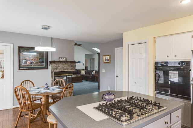 kitchen featuring pendant lighting, a fireplace, stainless steel gas stovetop, white cabinetry, and oven