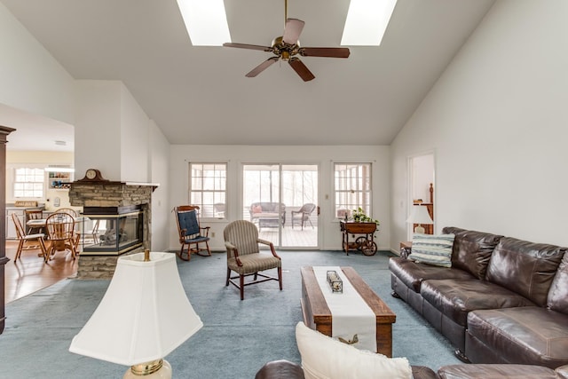 living area with high vaulted ceiling, a ceiling fan, carpet, a skylight, and a fireplace