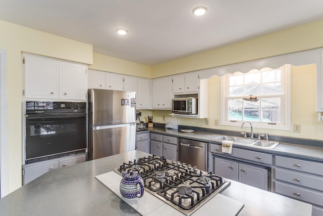 kitchen featuring dark countertops, gray cabinetry, white cabinets, stainless steel appliances, and a sink