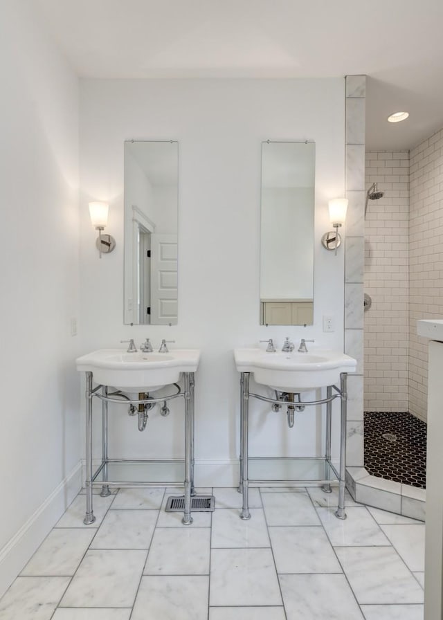 bathroom featuring dual sinks and tiled shower