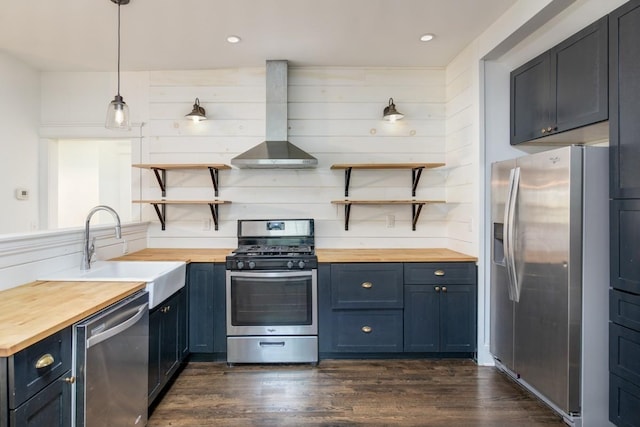 kitchen with sink, wall chimney range hood, wooden counters, appliances with stainless steel finishes, and decorative light fixtures