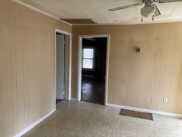 unfurnished room with ceiling fan, ornamental molding, and wooden walls