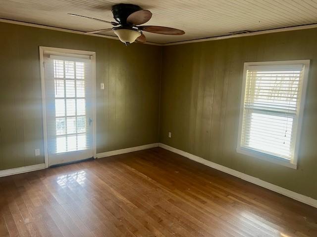 unfurnished room featuring wood-type flooring, ornamental molding, a healthy amount of sunlight, and wood walls