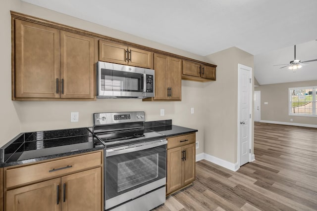 kitchen featuring appliances with stainless steel finishes, lofted ceiling, dark stone counters, ceiling fan, and light hardwood / wood-style flooring