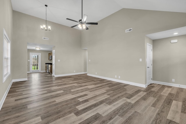 unfurnished living room with hardwood / wood-style flooring, ceiling fan with notable chandelier, and high vaulted ceiling