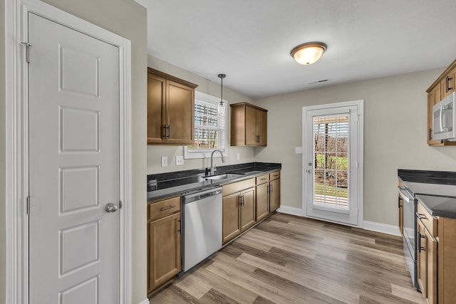 kitchen featuring appliances with stainless steel finishes, sink, light wood-type flooring, and decorative light fixtures