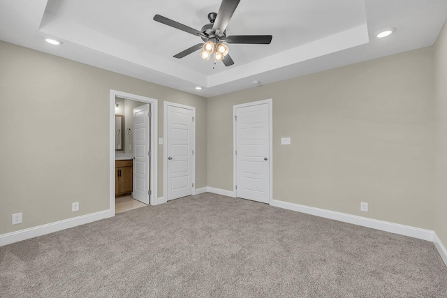 unfurnished bedroom featuring light carpet, connected bathroom, ceiling fan, and a tray ceiling