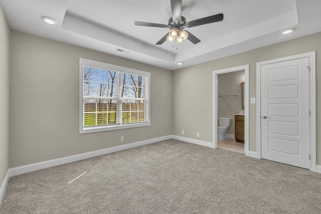 unfurnished bedroom with connected bathroom, light carpet, ceiling fan, and a tray ceiling