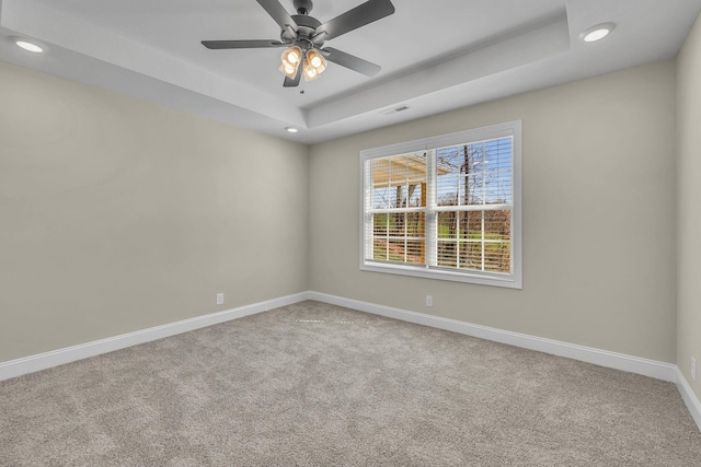 empty room featuring light colored carpet, a raised ceiling, and ceiling fan