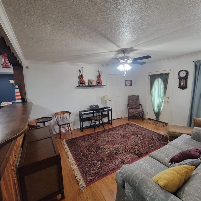 living room featuring ceiling fan, ornamental molding, hardwood / wood-style floors, and a textured ceiling