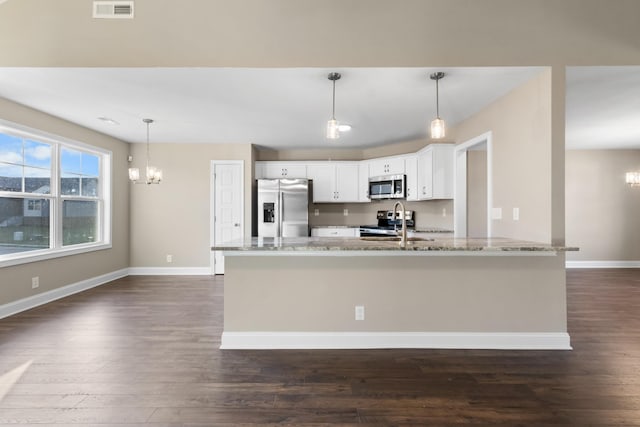 kitchen with appliances with stainless steel finishes, pendant lighting, white cabinets, light stone counters, and an inviting chandelier