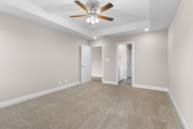 unfurnished bedroom with carpet flooring, connected bathroom, ceiling fan, and a tray ceiling