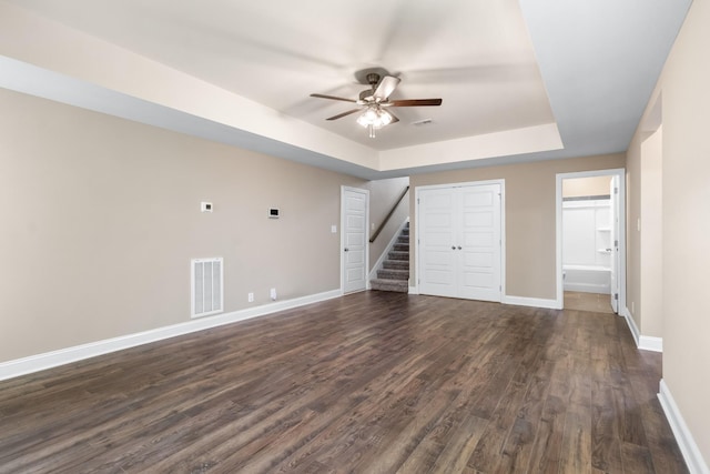 unfurnished living room with dark wood-type flooring, ceiling fan, and a tray ceiling