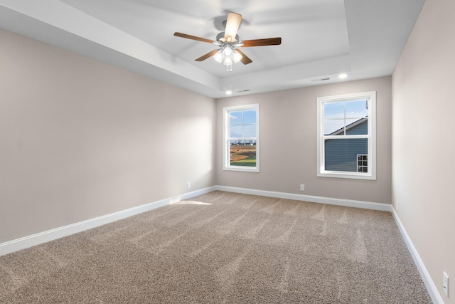 empty room with a raised ceiling, carpet floors, a healthy amount of sunlight, and ceiling fan