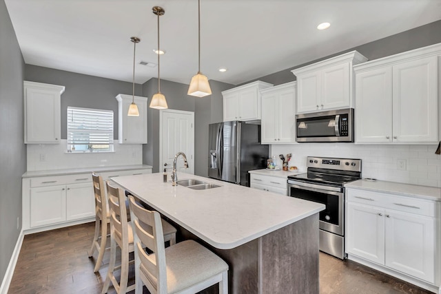 kitchen with a kitchen island with sink, hanging light fixtures, stainless steel appliances, and white cabinets